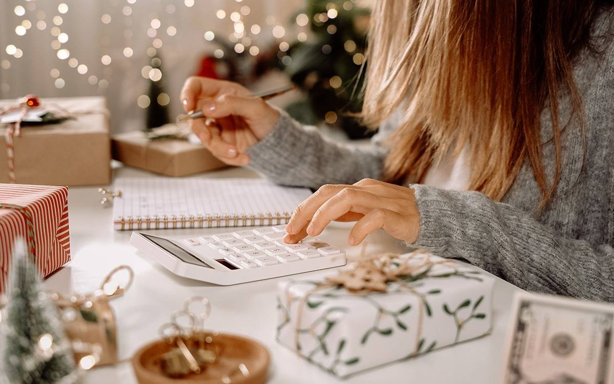 woman sitting at table with calculator and notepad, surrounded by Christmas gifts and decorations