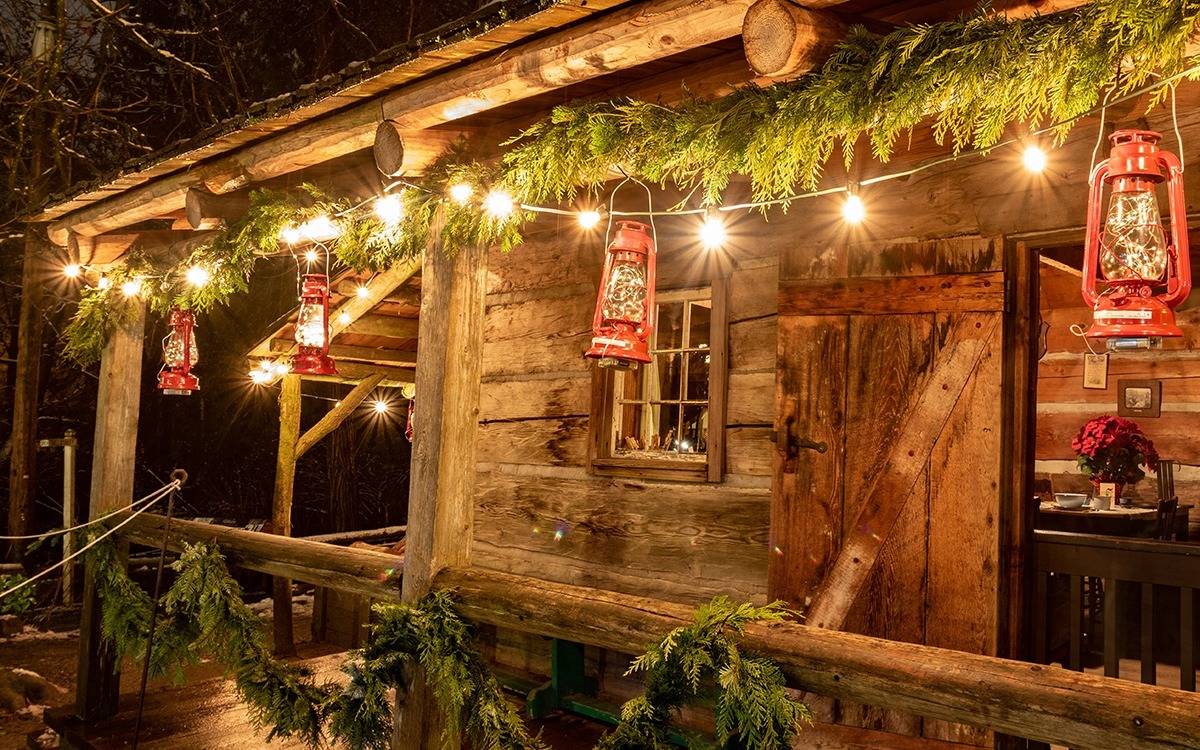 log cabin at night decorated with lighted pine garland and red lanterns