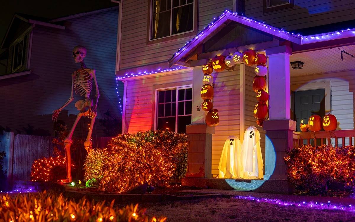 giant Halloween skeleton in front of house with orange and purple mini lights