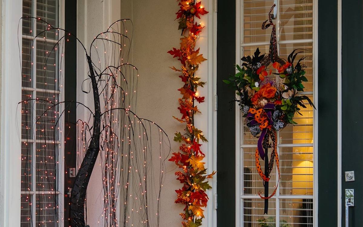 front porch with weeping lighted tree, leafy garland and Halloween wreath