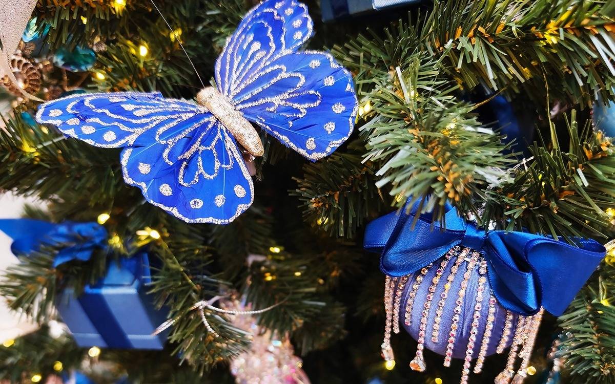 tree decorated with fanciful blue ornaments, blue and gold butterfly and blue wrapped gift ornaments