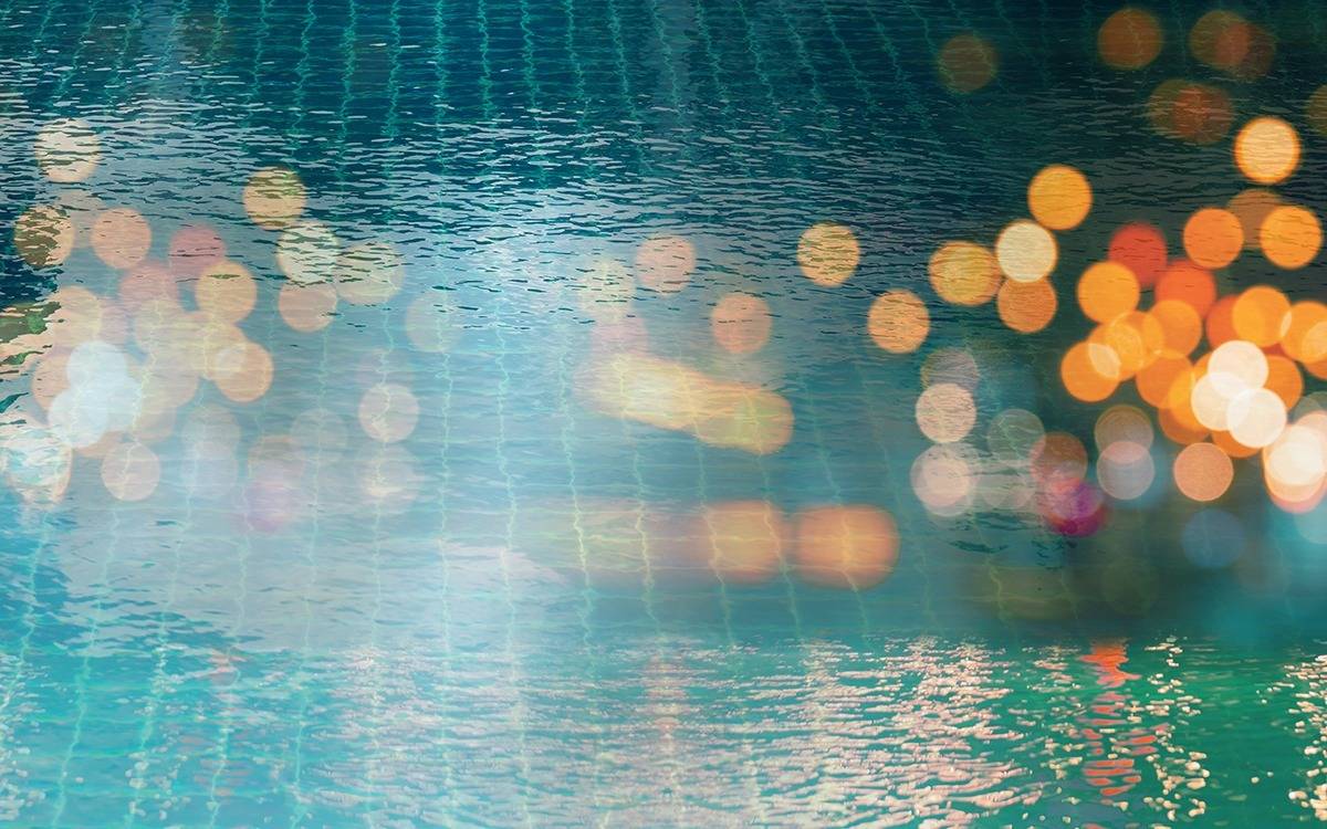 bokeh reflection of warm white patio lights in surface of calm swimming pool