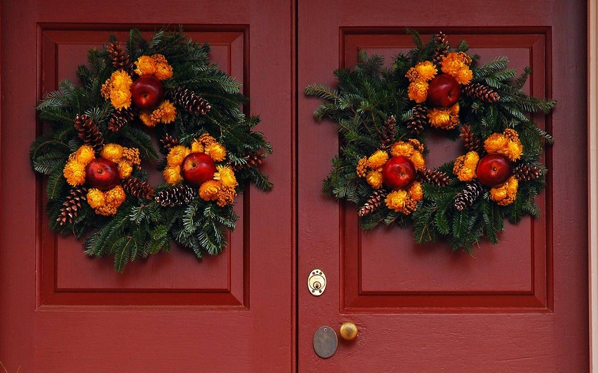 red entry doors with pair of pine wreaths decorated with apples, orange flowers and pinecones