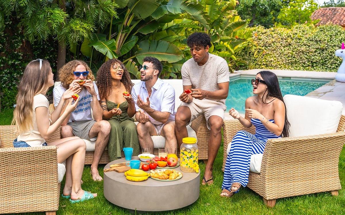 20-something friends seated around table full of food near swimming pool
