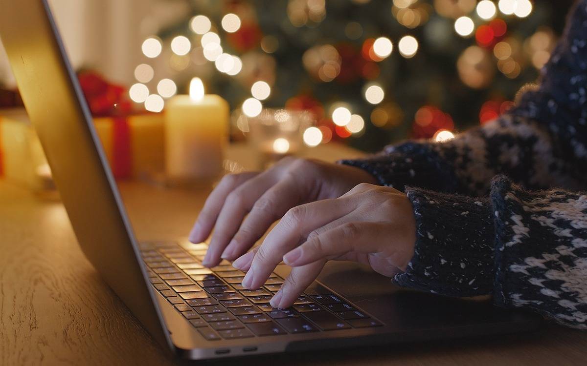 hands typing on laptop keyboard with blurred softly lit Christmas tree in background