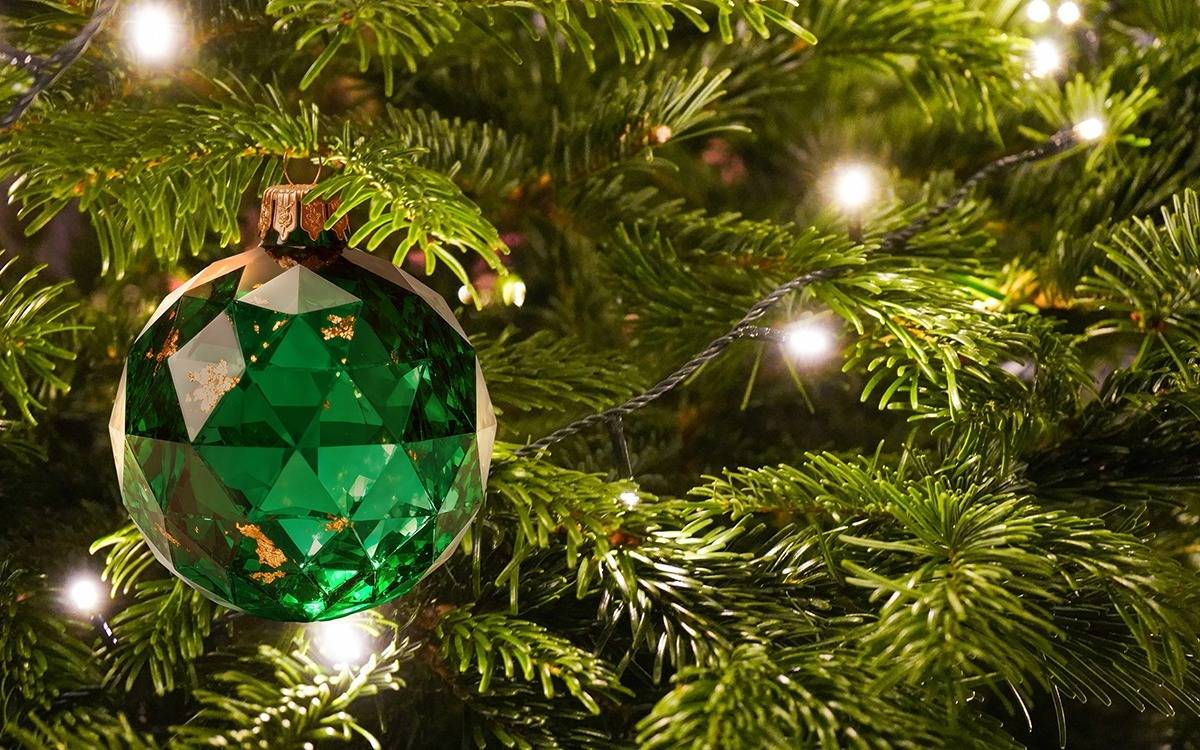 round, faceted, jewel-like ornament hanging on Christmas tree branches lit by white mini lights