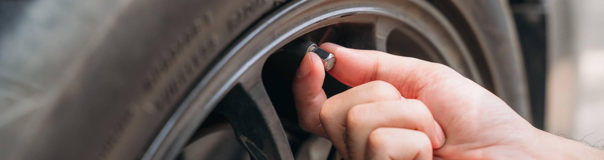Persons hand removing valve cap from valve on tire
