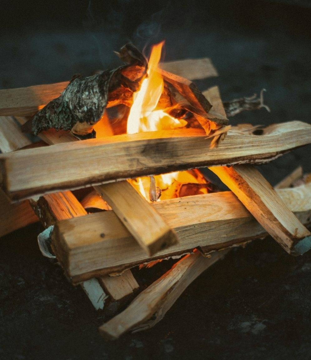 Log cabin shaped arrangement of wood with camp fire burning in the center