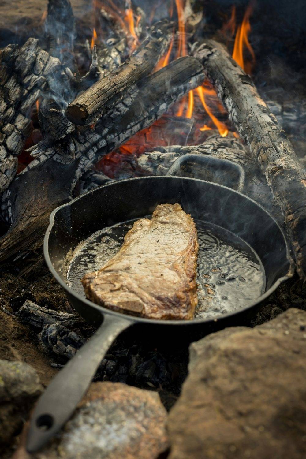 meat cooking in cast iron skillet over a campfire