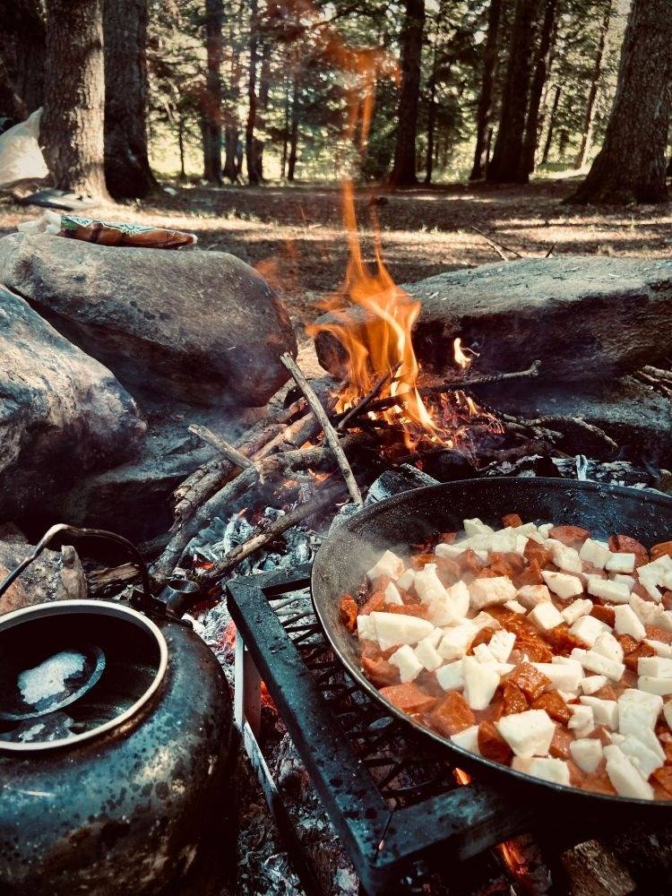 Campfire cooking setup with cast iron skillet, teapot, grilling grate and secondary fire
